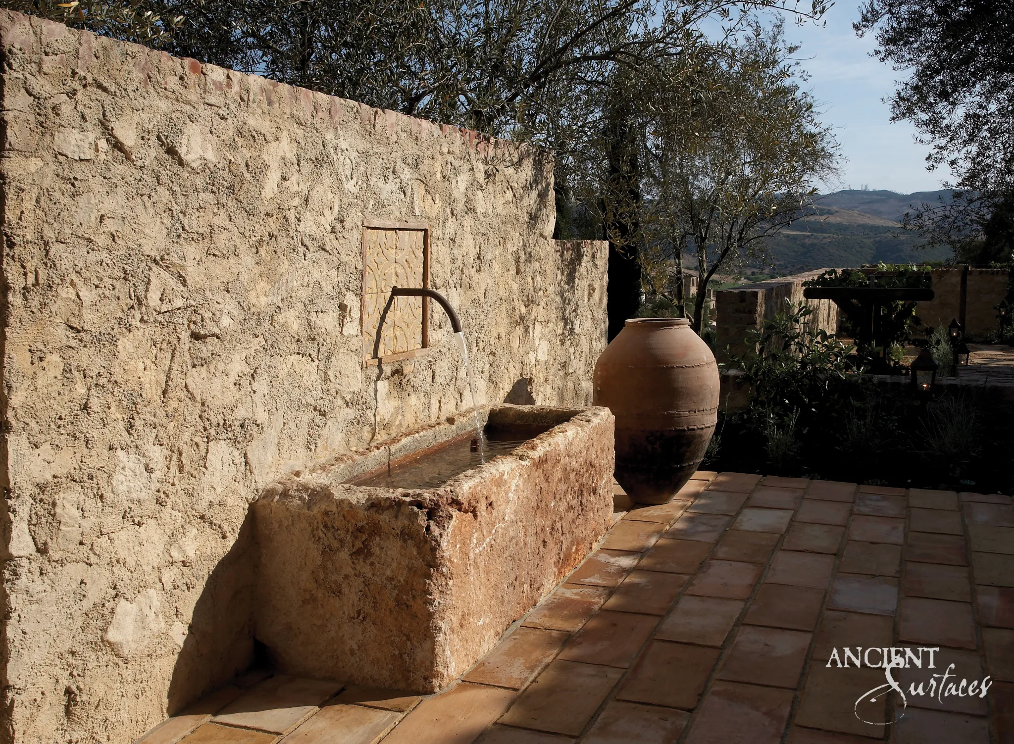Rustic reclaimed limestone trough fountain flowing on a sunlit Mediterranean terrace