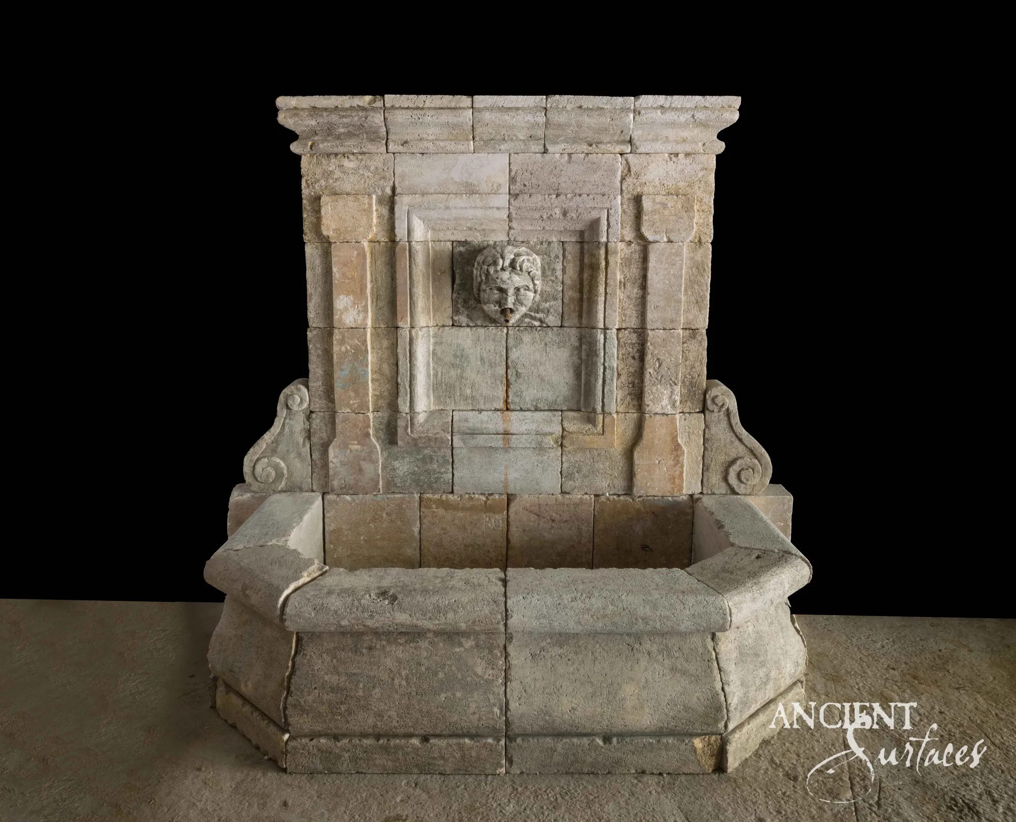 Large reclaimed limestone wall fountain with a carved mask spout and deep stone basin
